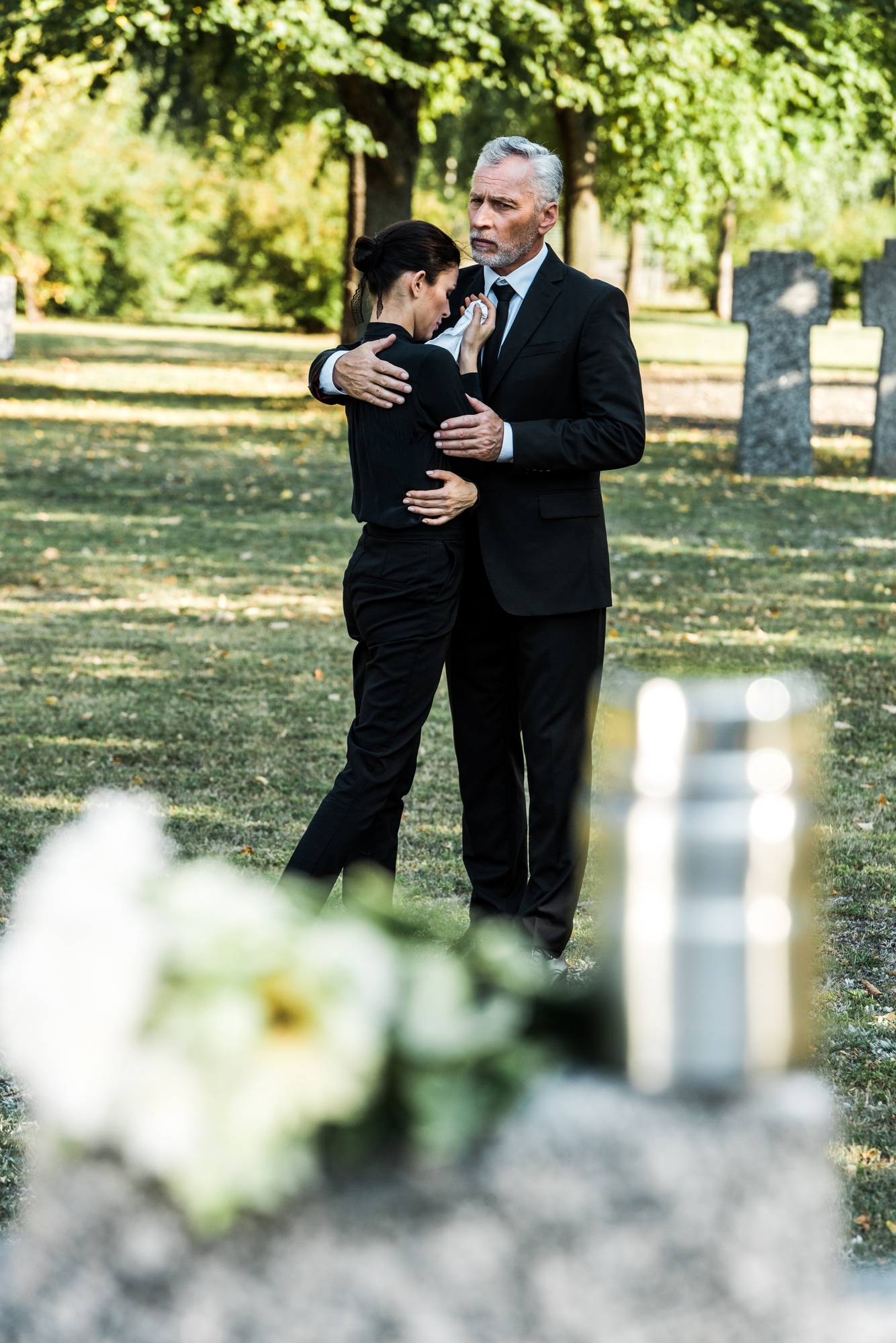 selective focus of senior man hugging upset woman in cemetery