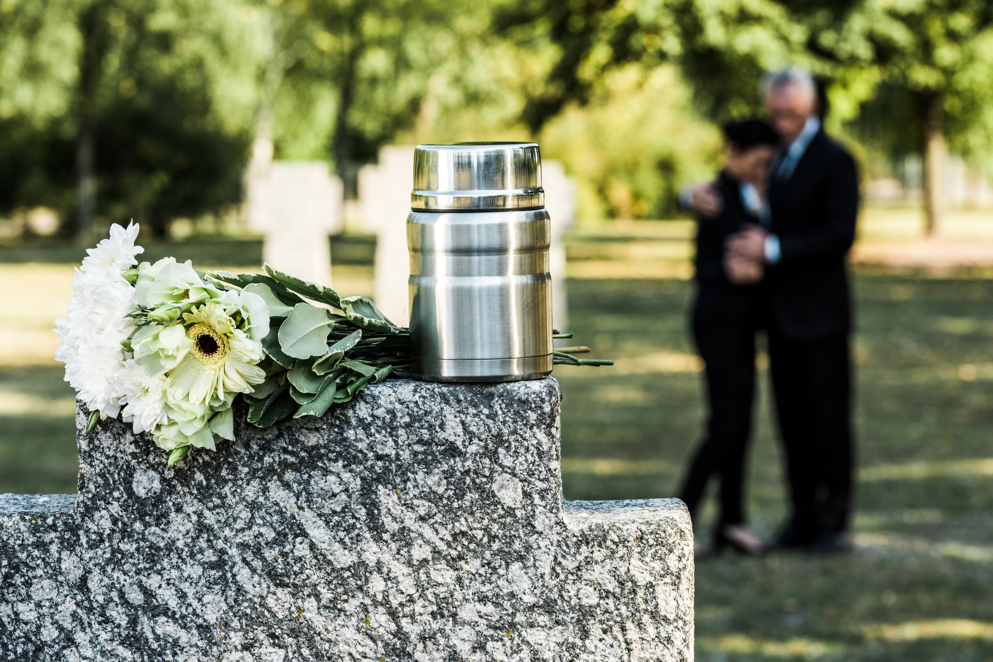 selective focus of white flowers and cemetery urn on tombstone